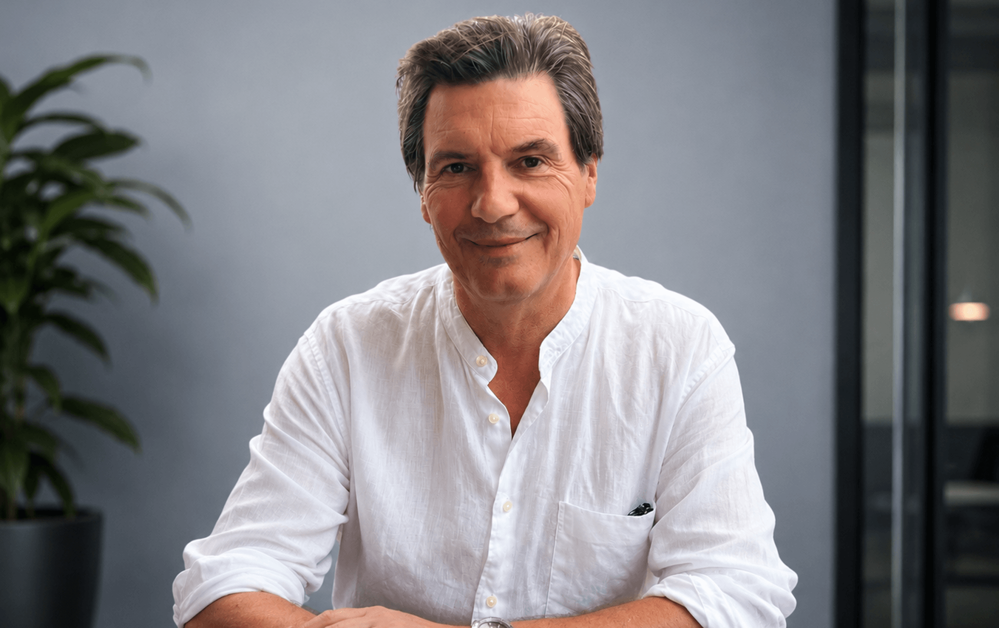 Portrait of a middle-aged man with brown hair wearing a white shirt against a gray background with a plant