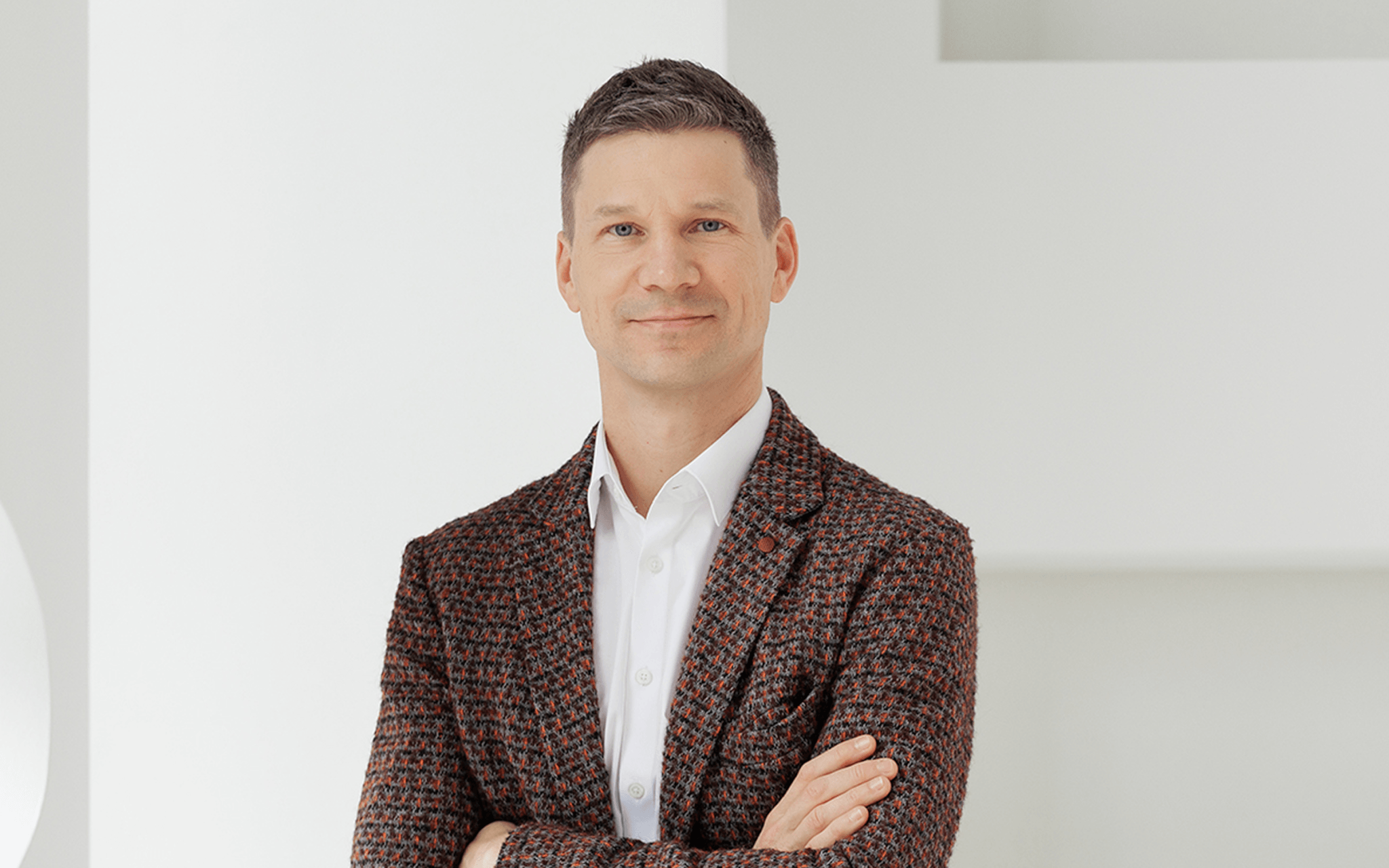 A professional portrait of a man wearing a red tweed blazer and a white shirt against a neutral background.