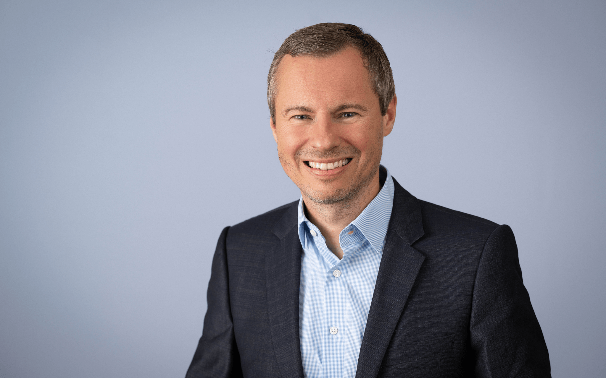 Professional portrait of a man in a dark suit and light blue shirt against a neutral background